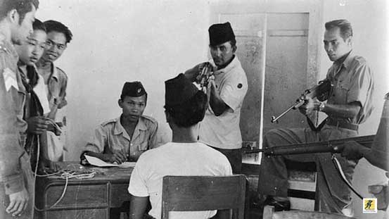 Teks foto ini menjelaskan sejumlah tentara tengah memeriksa, seraya menodongkan senapan, seseorang yang disebutkan sebagai bagian tentara pro-PKI tidak lama setelah peristiwa Madiun 1948.