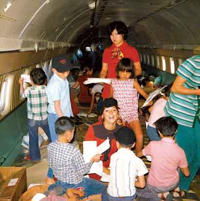 Pramugari World Airways, Carol Shabata (berdiri) dan Valerie Witherspoon (berlutut) bermain bersama anak-anak yatim piatu Vietnam dalam penerbangan evakuasi bersejarah tersebut.