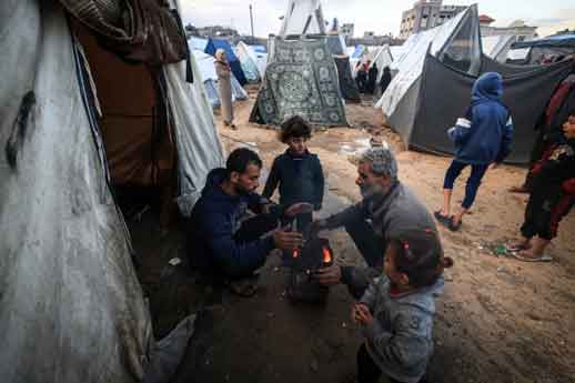 Pengungsi Palestina mencoba melakukan pemanasan di sekitar api unggun di tengah tenda-tenda yang terendam air hujan lebat di Rafah di Jalur Gaza selatan.