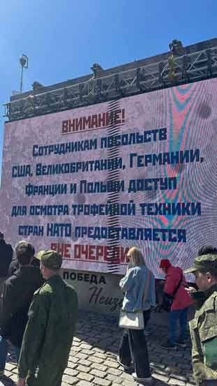 Foto dari pameran piala perang baru-baru ini di Moskow. Papan reklame itu berbunyi: “Pegawai kedutaan besar AS, Inggris, Jerman, Prancis, dan Polandia diperbolehkan memasuki pameran senjata piala NATO tanpa mengantri.”